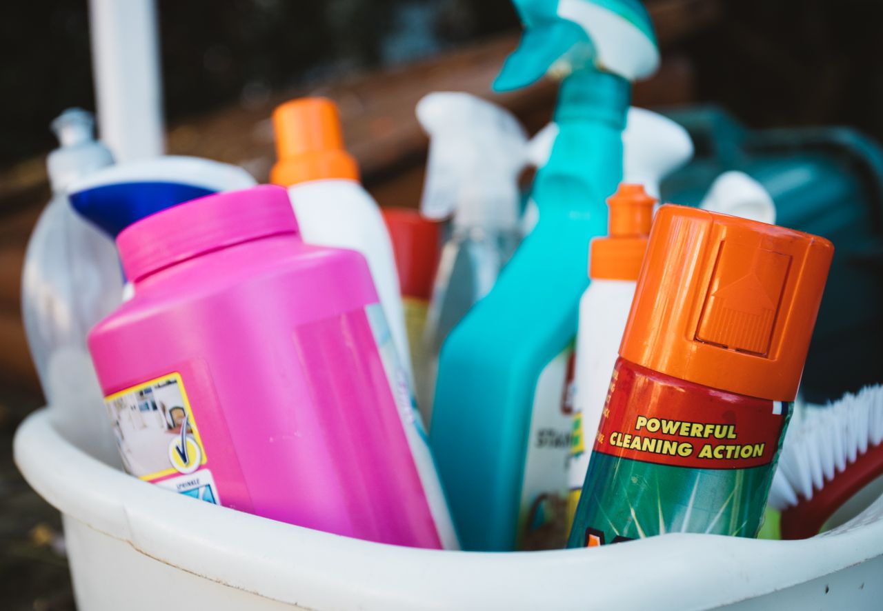 services-01 Close-up of assorted cleaning supplies in a bucket outdoors, showcasing various detergents and sprays.