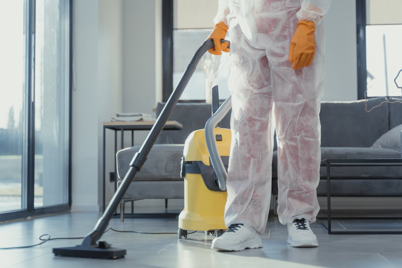 gallery-6 A cleaner in protective coveralls and gloves vacuuming a modern living room.