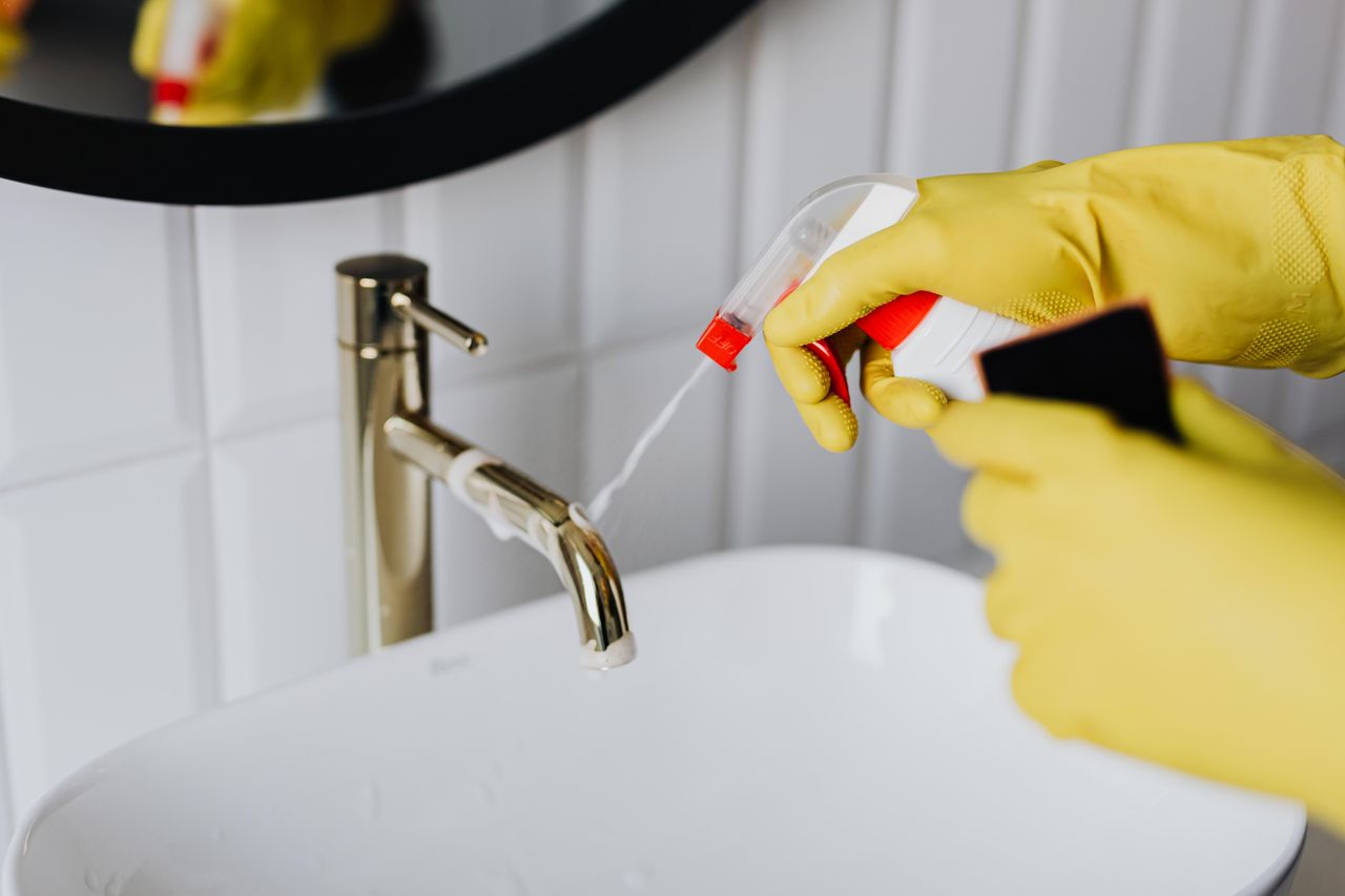 about-01 From above anonymous housekeeper in yellow rubber gloves spraying cleaner to chrome water faucet in bathroom